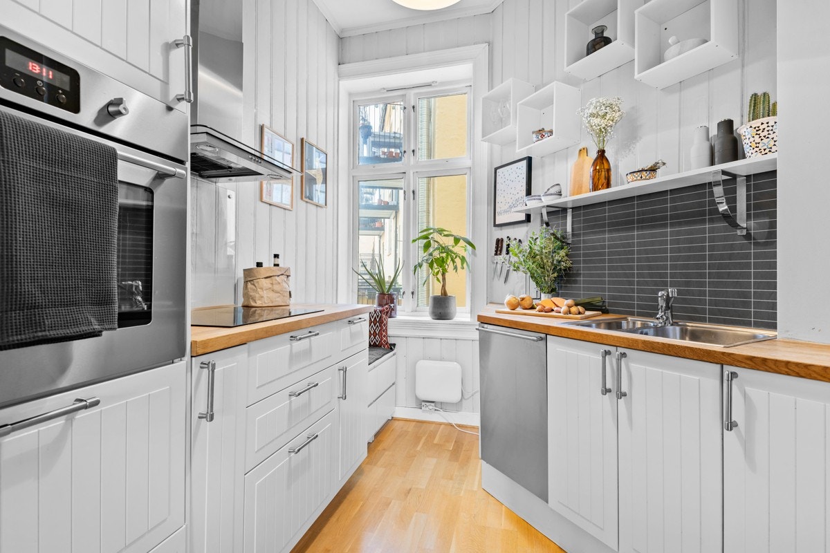 Kjøkkeninnredningen består av hvite profilerte fronter, heltre benkeplate, rustfri servant, ventilator, nisje for kjøleskap og oppvaskmaskin, glass- og aluplater over benkeskap. Galleribilde