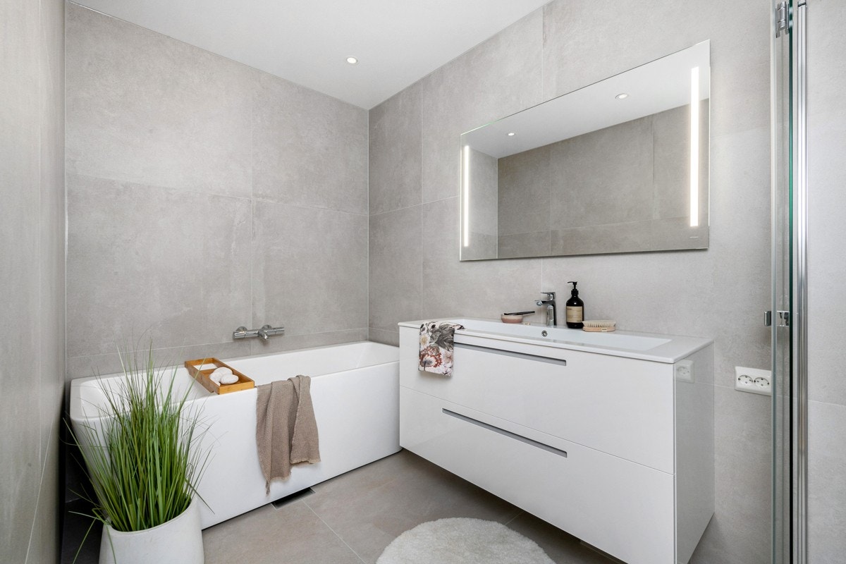 Det andre badet har servant i seksjon med lys/speil, dusj på vegg bak glassdører og et badekar. Galleribilde