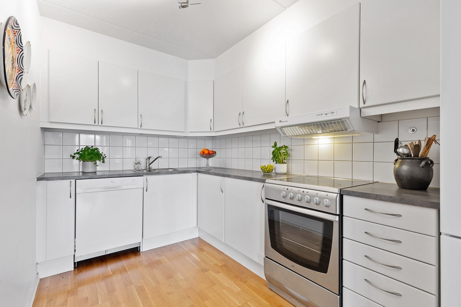 Hvite glatte fronter, laminat benkeplater, oppvaskkum, ventilator og fliser over benk. Galleribilde