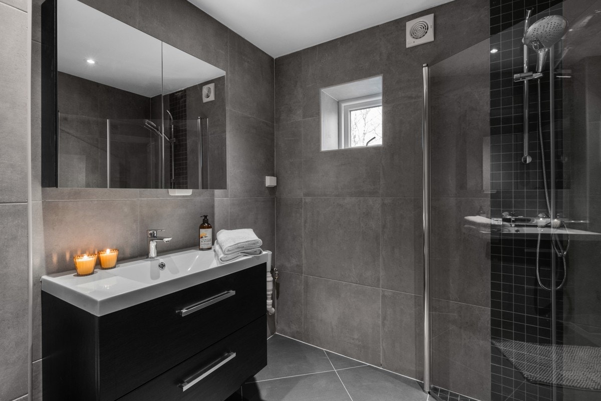 Baderomsinnredningen har finerte, grå fronter og består av en heldekkende servant på en skuffeløsning og et dobbelt speilskap. Galleribilde