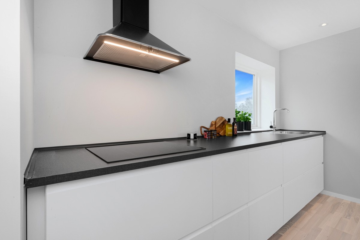 Innredningen har hvite, glatte fronter, takhøye skap og mørkegrå laminatbenkeplate. Galleribilde