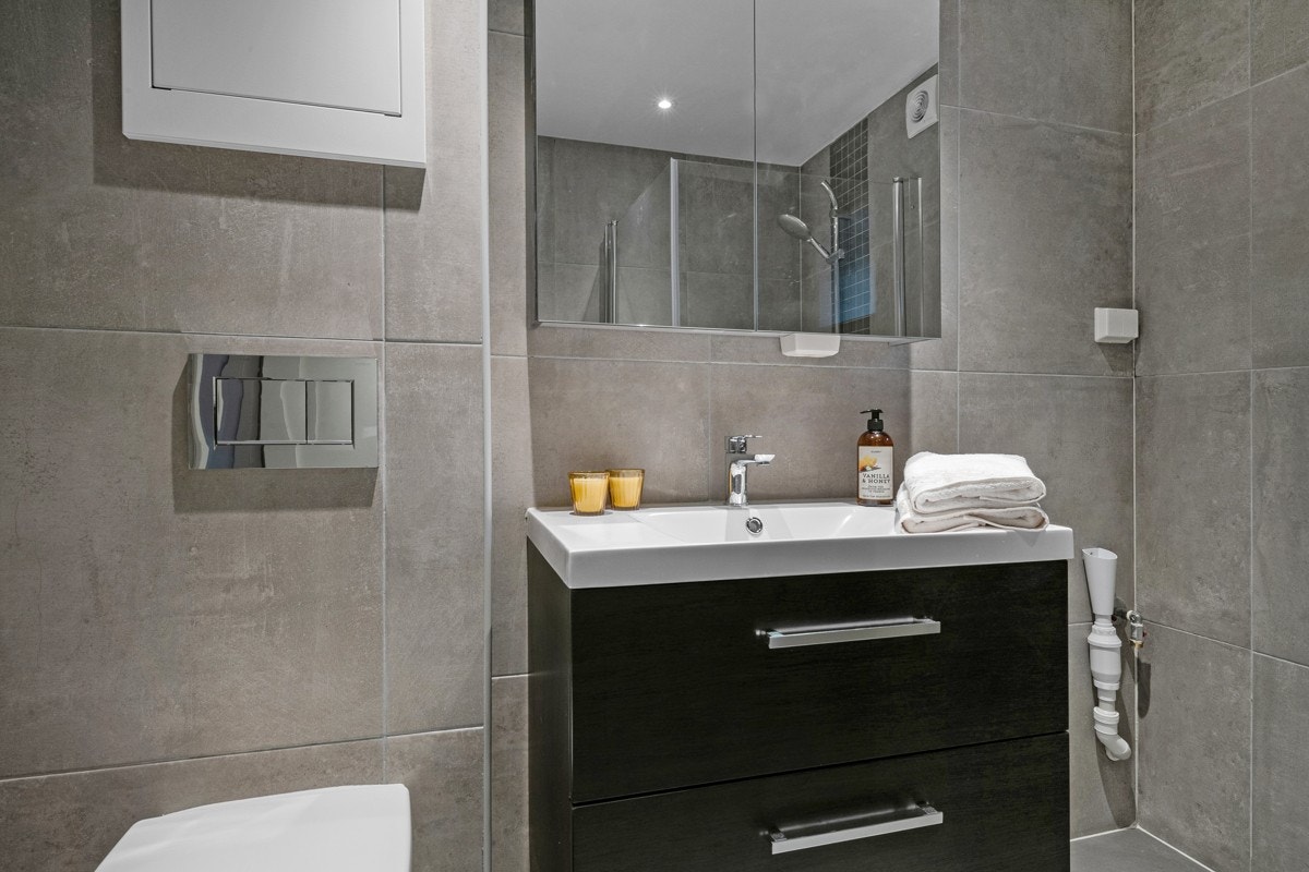 Videre har badet et vegghengt toalett, opplegg for vaskemaskin og et dusjhjørne med innfellbare glassdører. Galleribilde