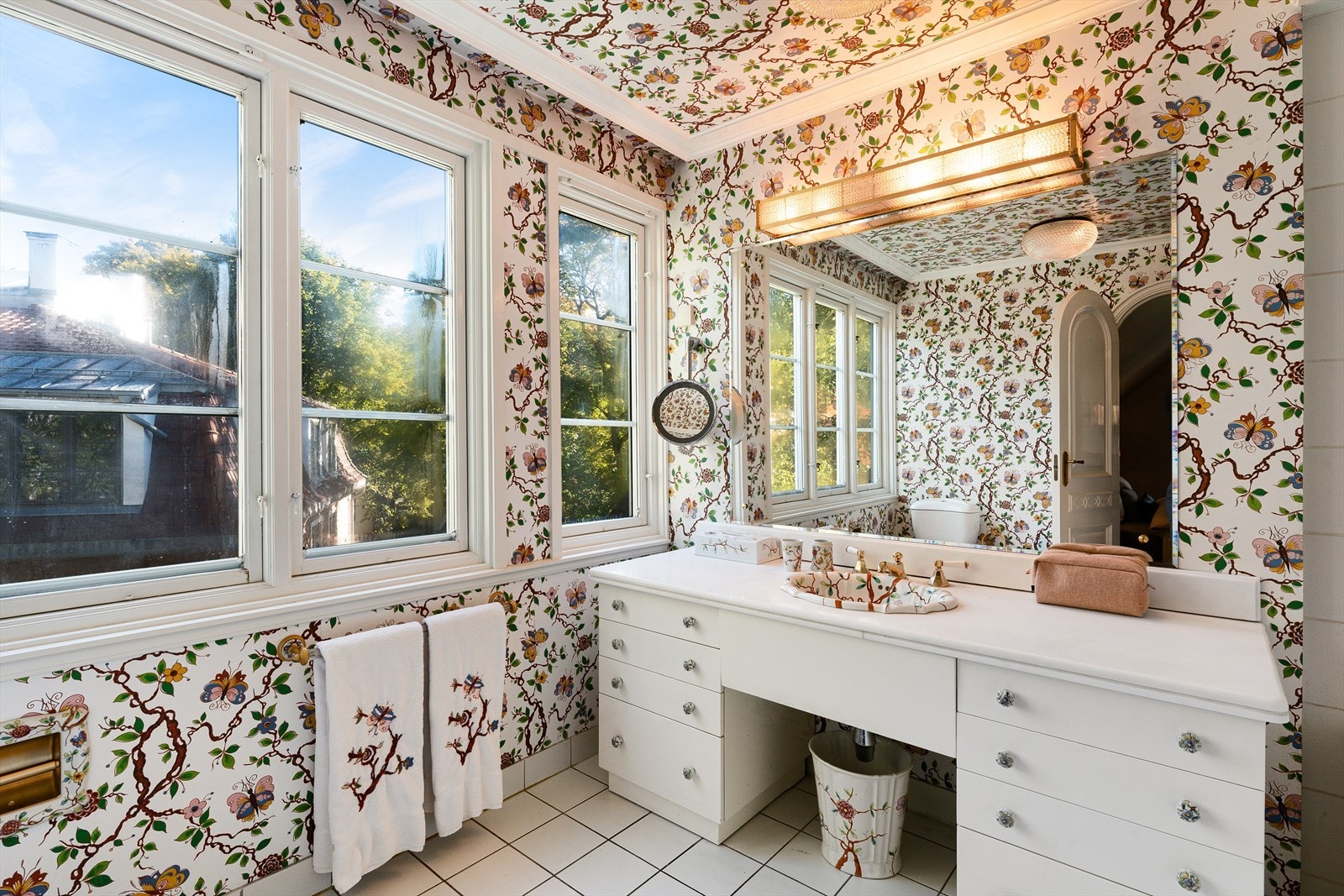 Baderom med adkomst fra hovedsoverom. Flislagt gulv og tapet på vegger. Galleribilde