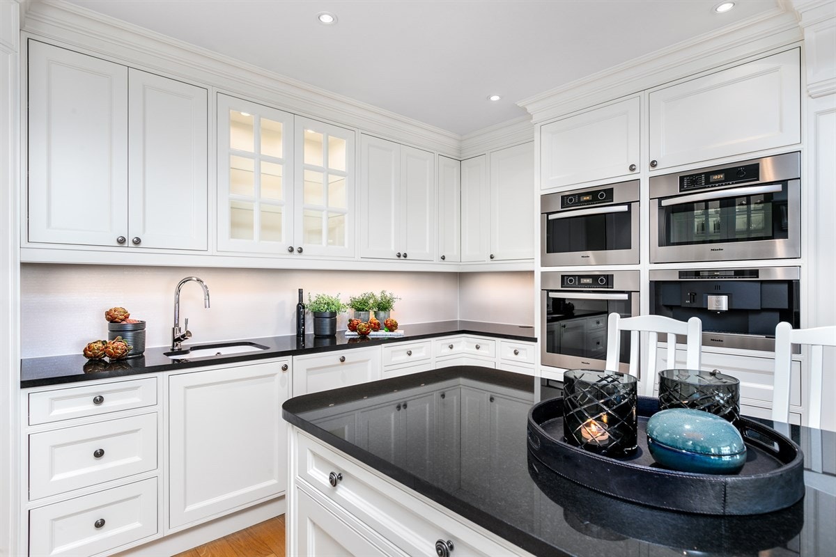 Innredningen har hvite profilerte fronter samt vitrineskap med lys. Lekker kvalitetsbenkeplate i svart granitt med oppvaskkum i porselen fra Villeroy & Boch med ett-greps blandebatteri med uttrekk. Galleribilde