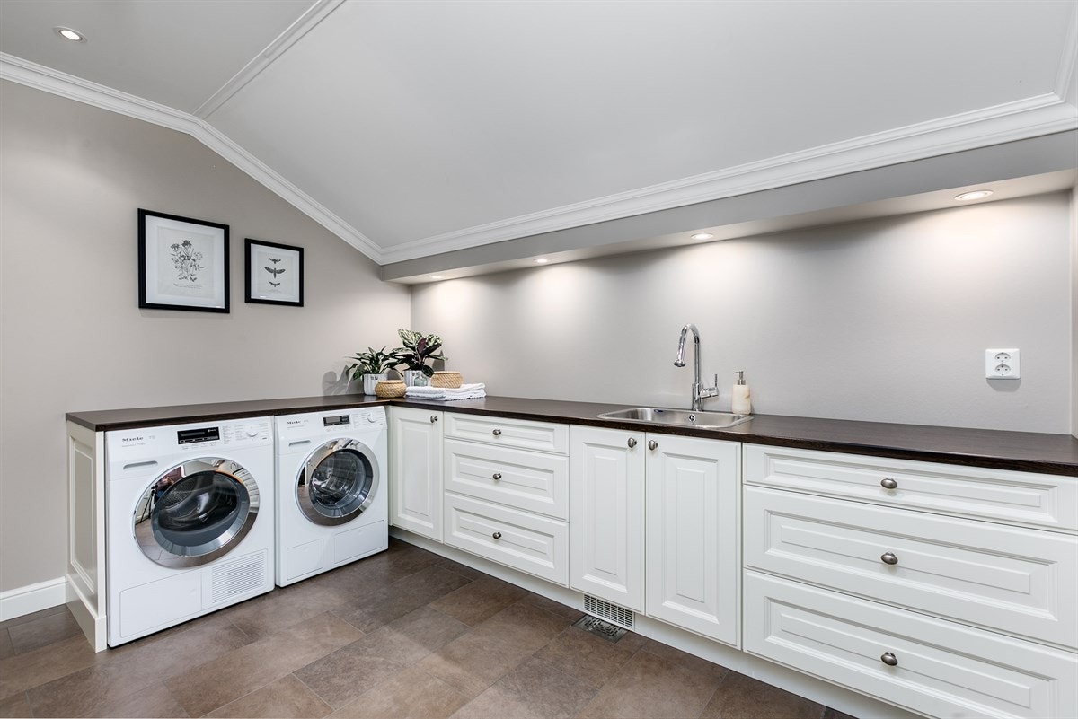 Praktisk og innbydende vaskerom med egen inngangsdør. Innredning fra JH Interiør med flere skap og skuffer, samt kum fra med ett-greps blandebatteri fra Hansgrohe med uttrekk. Rommet har opplegg for vaskemaskin. Galleribilde
