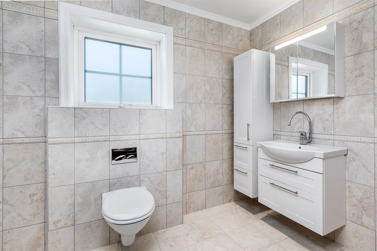 Lekkert bad i sekundærleilighet med italienske fliser fra Panaria Ceramica. Baderomsmøbel fra Aspen med servant og skuffer, veggskap og speilskap med belysning. Videre har badet nedfelt dusjhjørne og vegghengt toalett samt opplegg for vaskemaskin. Galleribilde
