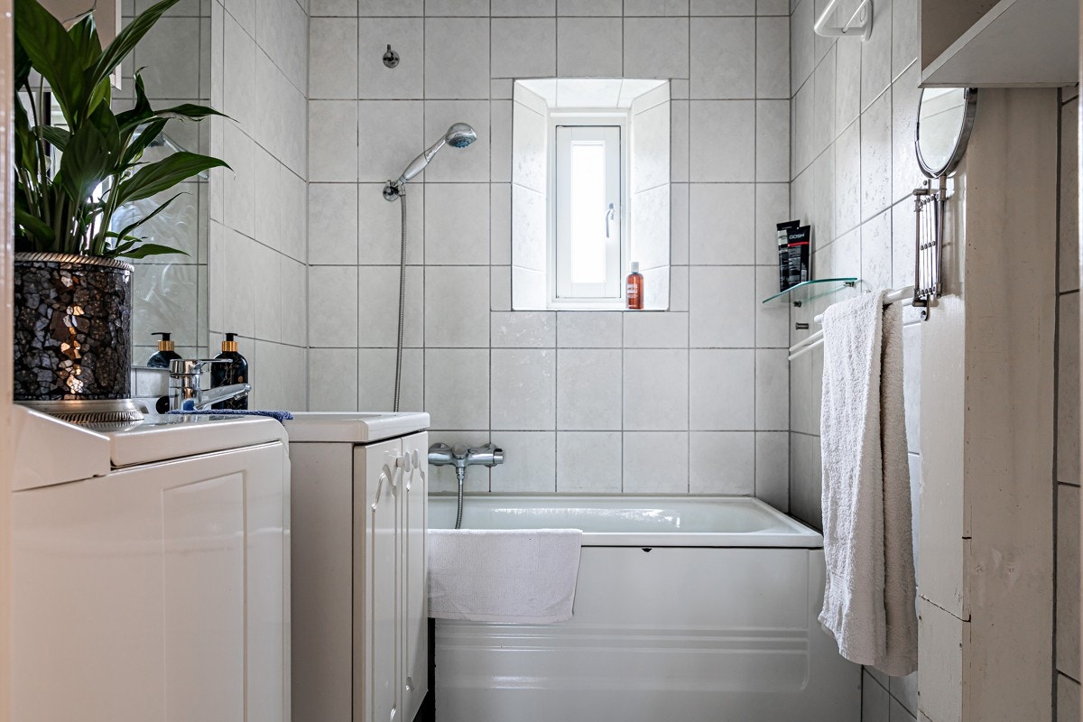 Flislagt bad med badekar, opplegg for vaskemaskin og vindu som slipper inn naturlig lys Galleribilde