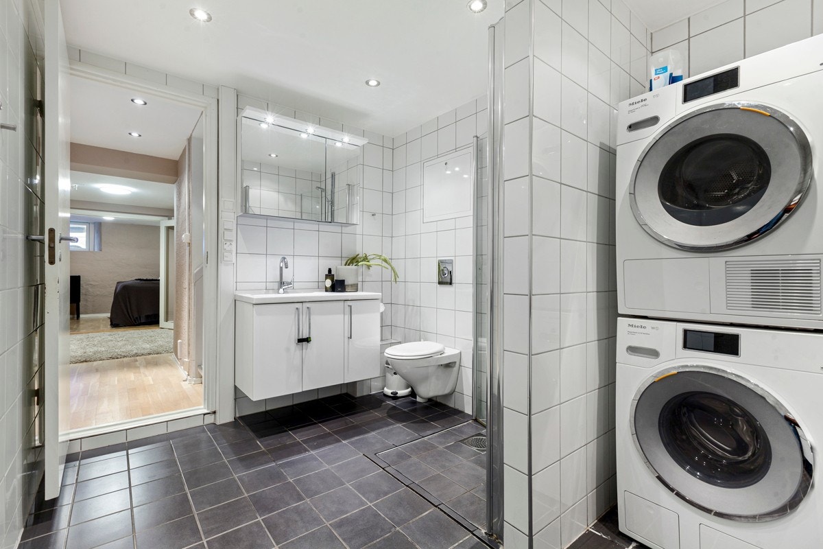Her er det god plass til vaskemaskin og tørketrommel. Videre er det en praktisk arbeidsbenk med over veggskap med fronter i hvit høyglans på endevegg. Varmtvannsbereder på 200 liter er plassert innerst i rommet Galleribilde
