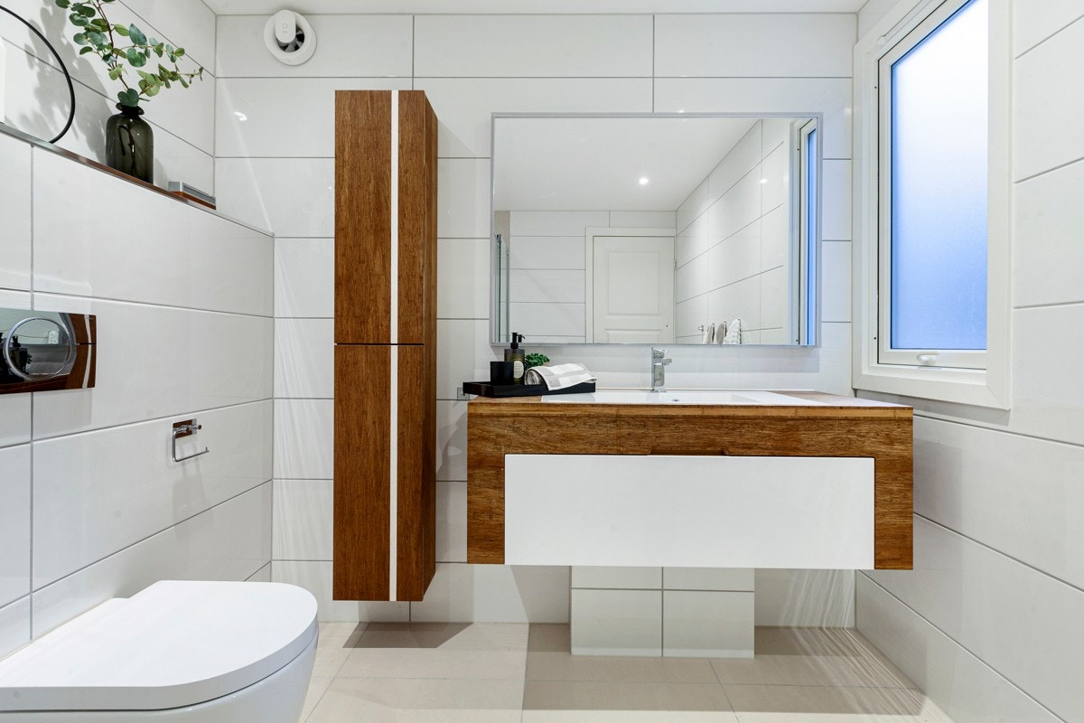 Innredningen består av skap med skapstamme og benkeplate i tre med nedfelt hvit servant, skuffefronter i hvit høyglans, speil på vegg over servant, samt høyskap i bambus med heltre hyller Galleribilde