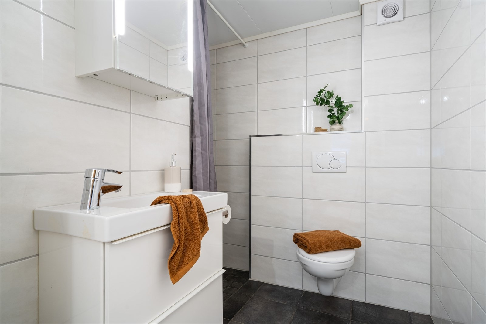 Badet er helfliset med fliser i tidløse farger. Sanitærutstyr er: vegghengt toalett, dusj og servant med innredning. Galleribilde