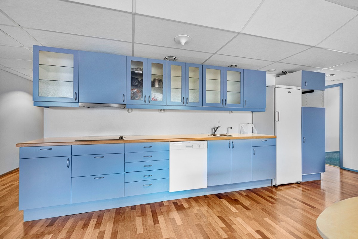 Kjøkkenet i første etasje har vitrineskap og blå, glatte fronter. Benkeplaten er laminert med platetopp og nedfelt kum. Galleribilde