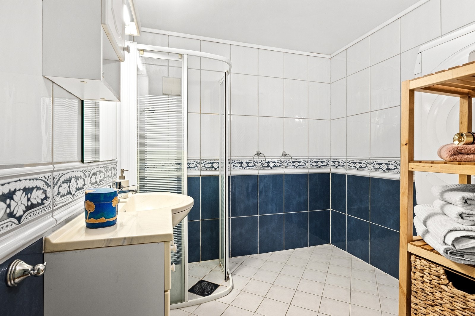 Flislagt baderom med heldekkende servant, underskap, dusjhjørne og opplegg for vaskemaskin og tørketrommel. Varme i gulv Galleribilde