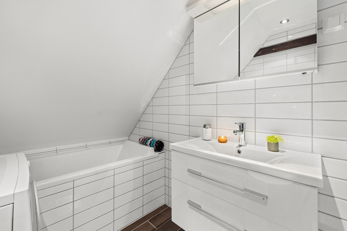 Badet har innfliset badekar med dusj, separat dusj med svingbare dusjdører i glass, veggmontert klosett fra Villeroy & Boch, heldekkende servantplate, baderomsinnredning og speilskap. Det er også opplegg for vaskemaskin. Galleribilde