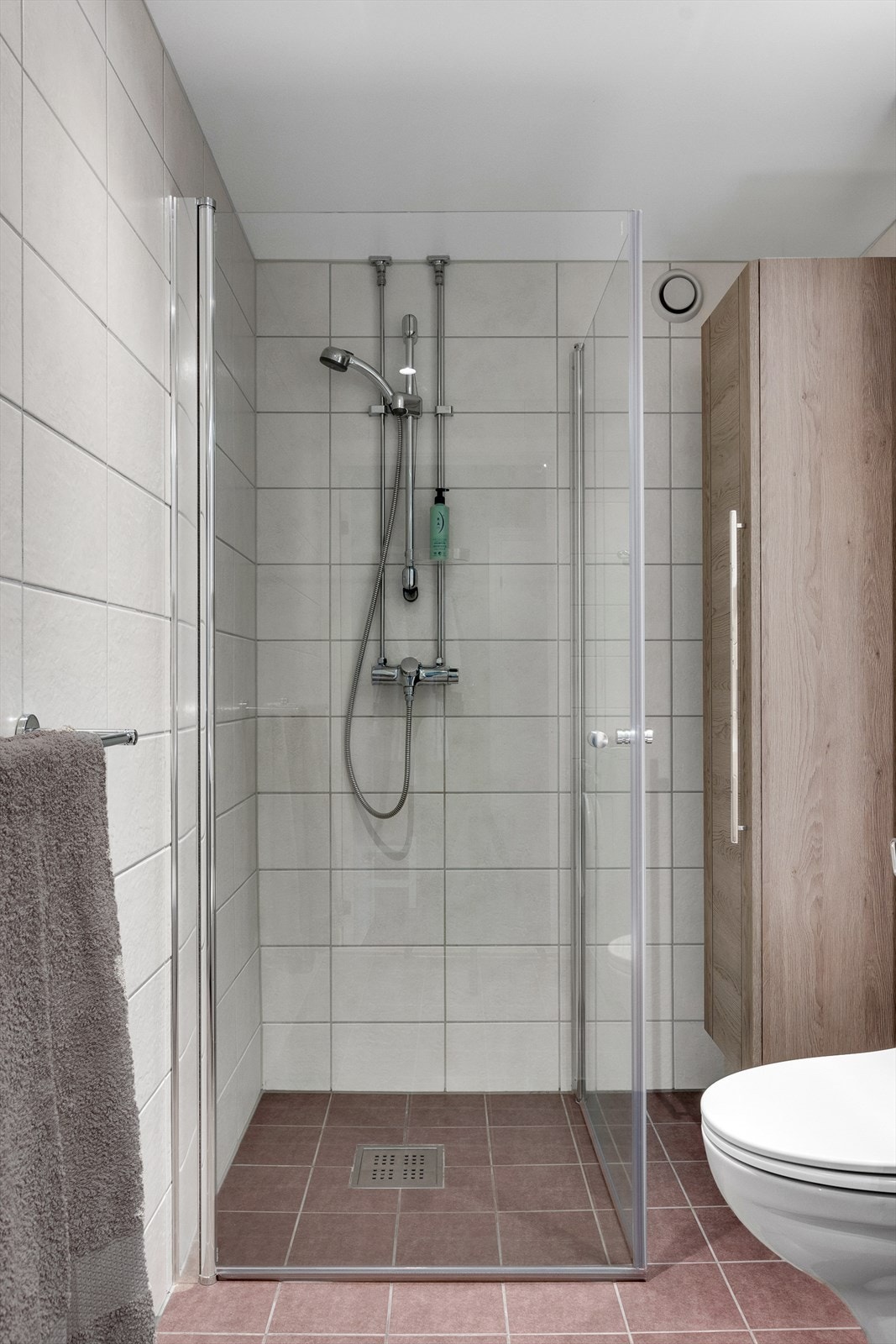 Baderommet er innredet med vegghengt toalett, servantskap med glatte fronter og dusjnisje med innfellbare glassdører. Galleribilde