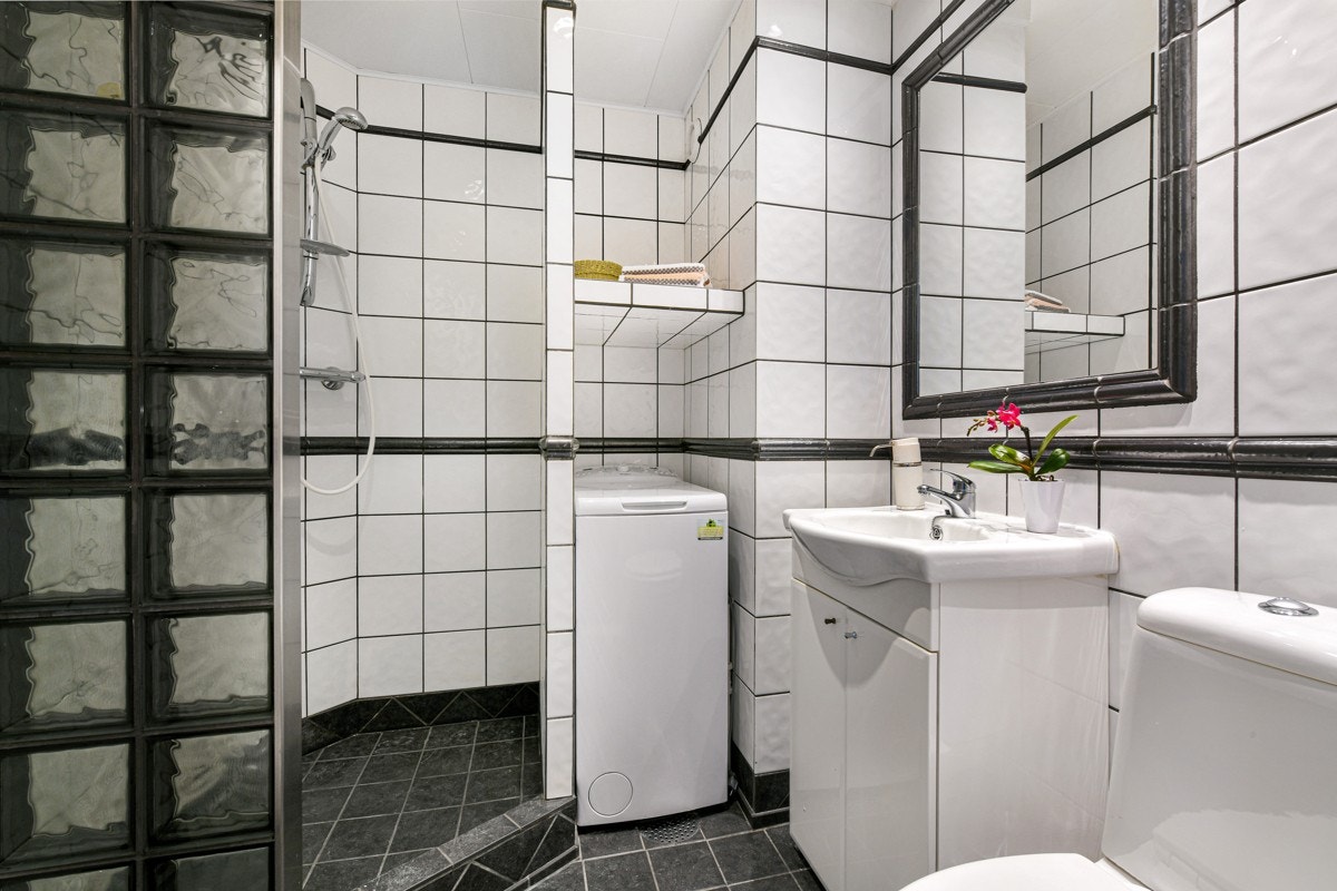 Badet er pent og praktisk, med grå fliser på gulvet og hvite fliser på veggene. Galleribilde