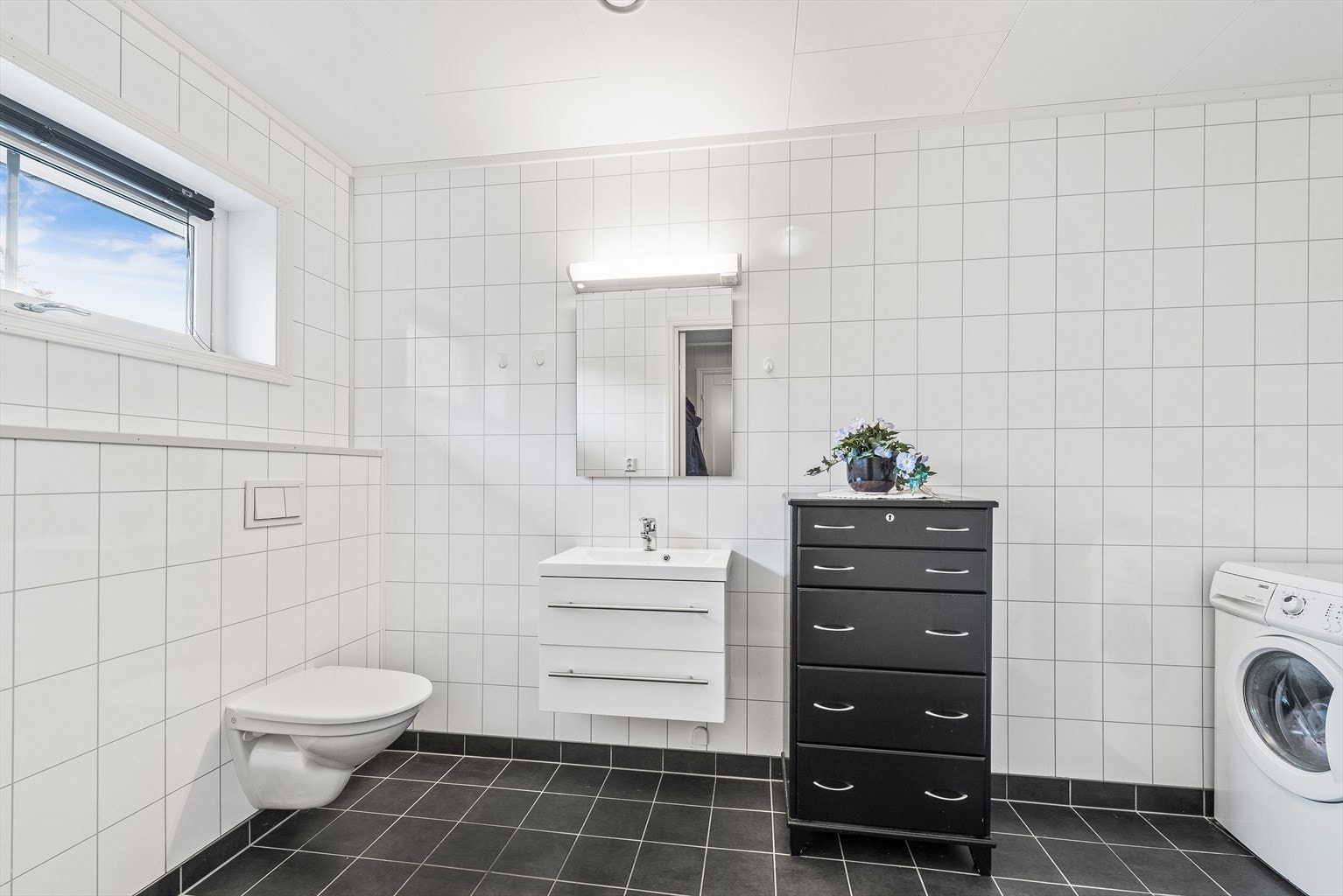Vaskerommet er flislagt og utstyrt med opplegg for vaskemaskin, vegghengt toalett og servant med skap. Galleribilde