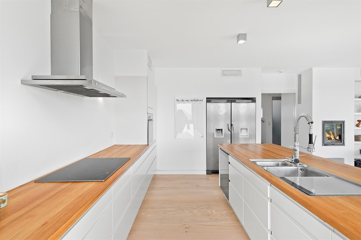 Induksjonsplatetopp, kaffemaskin, stekeovn, oppvaskmaskin og vinskap er integrert, og det er nisjer til kjøleskap og fryser Galleribilde