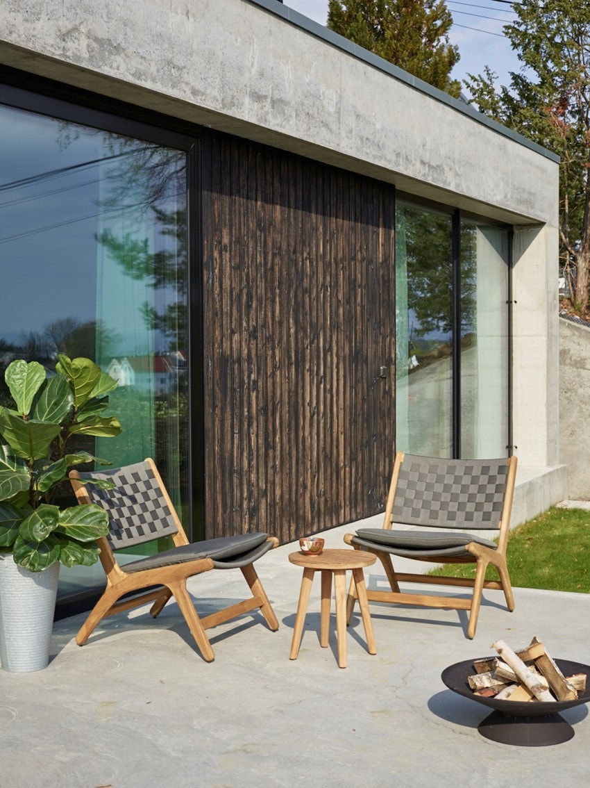 Utenfor stuen er det markterrasse i stålglattet betong, tilliggende plenareal innrammet av grønne planter. Galleribilde