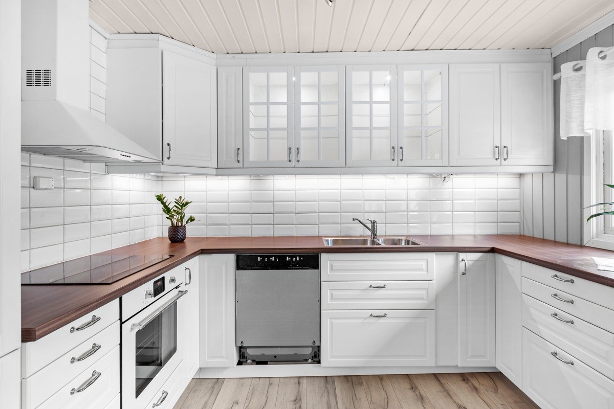 Innredningen er oppforet og har hvite, profilerte fronter, vitrineskap med lys, benkebelysning, hvit fliser under overskap og laminerte benkeplater med halvannen kum. Galleribilde