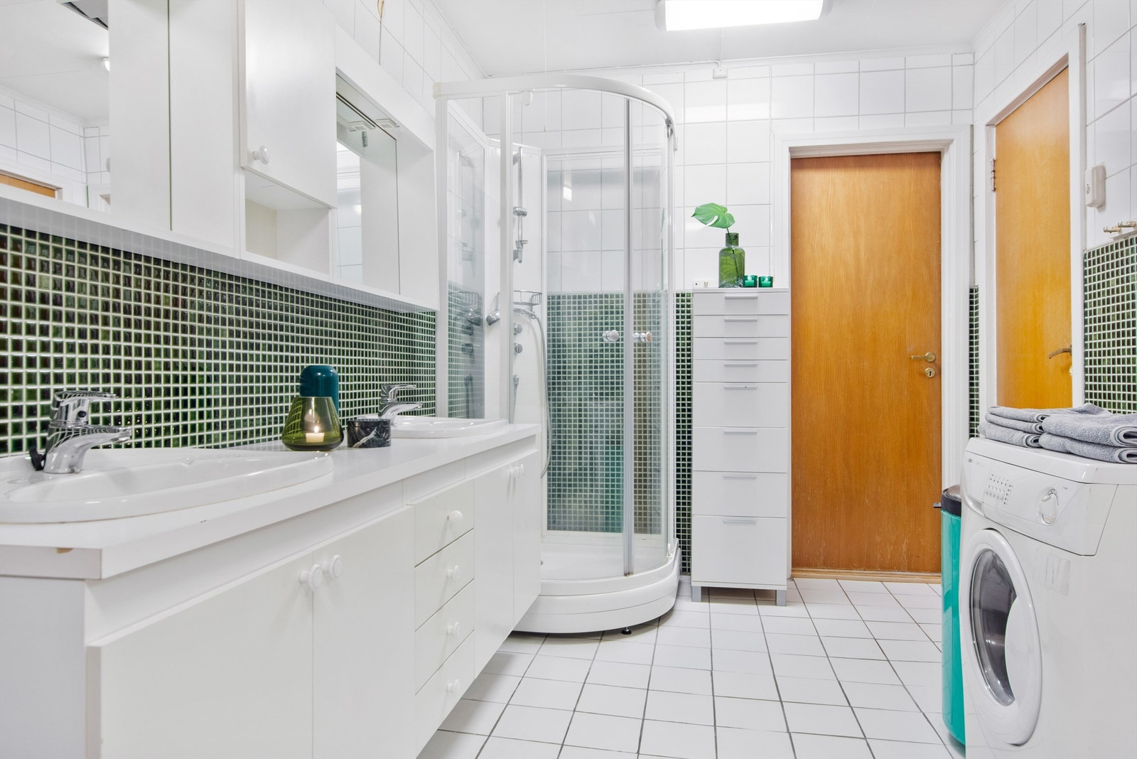 Lyst og rosmlig bad med dobbelvask, dusjkabinett og opplegg for vaskemaskin. Galleribilde