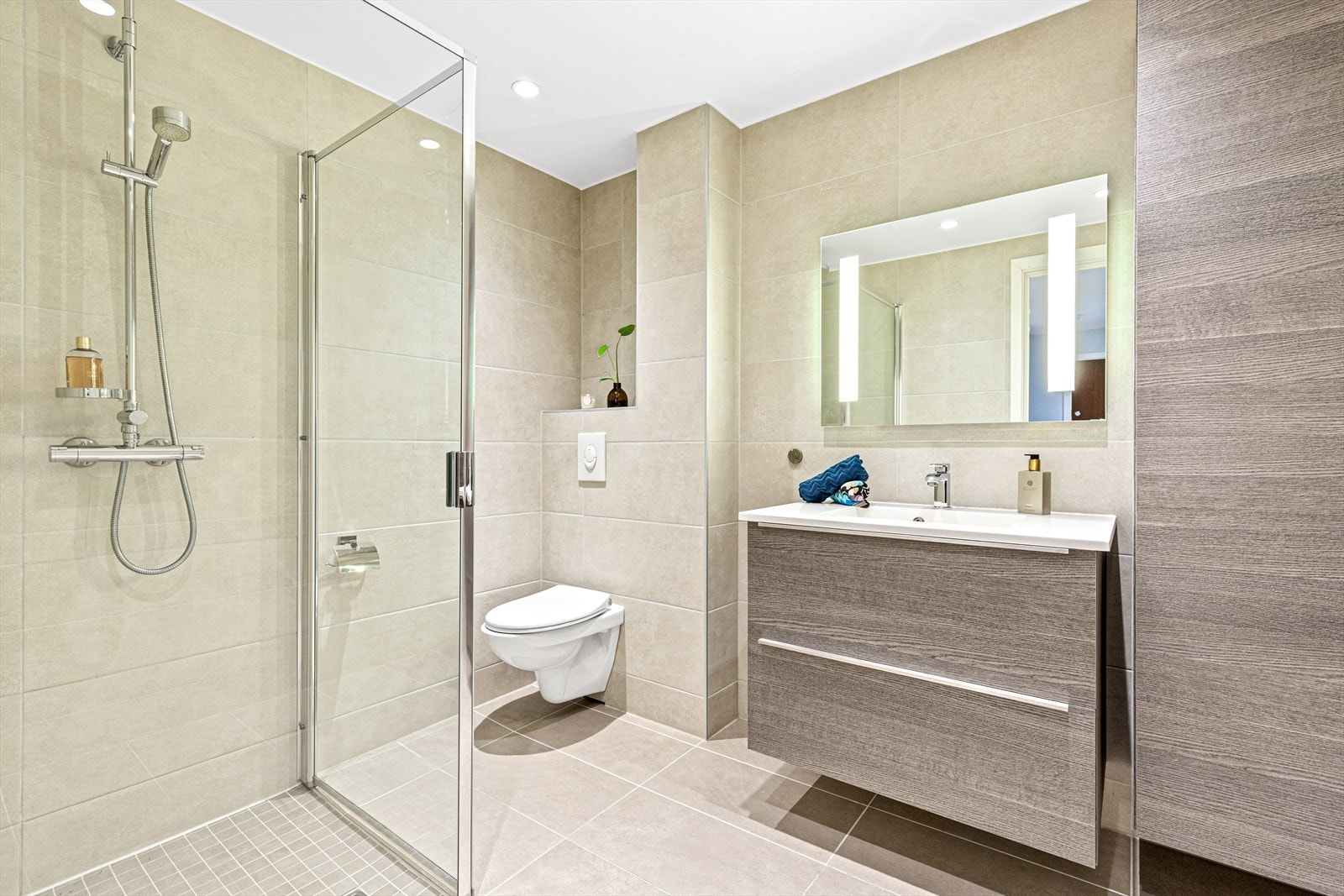 Flott bad (2014) med dusjnisje hvor det er montert regnfallsdusj og glassvegger, veggmontert wc, høyskap og servant med dyp skuffeinnredning Galleribilde