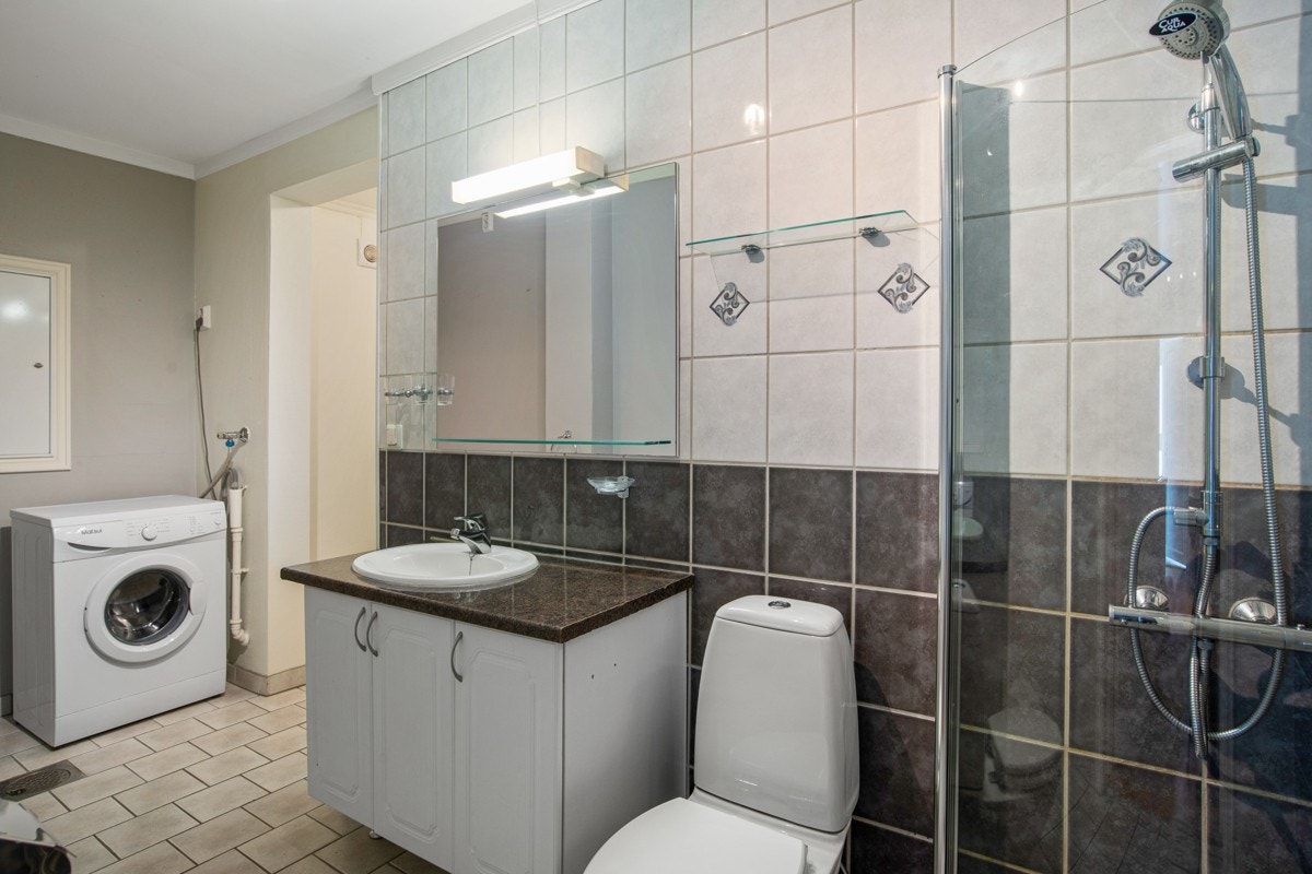 Badet som tilhører hybelen har flislagte overflater i tofarget kombinasjon, gulvvarme, frittstående toalett og deilig regnfallsdusj bak innfellbare glassdører. Innerst i rommet er det opplegg for vaskemaskin og tørketrommel. Galleribilde