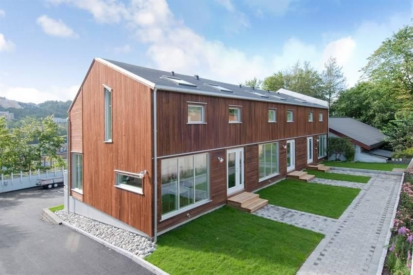 Fasade bak, inngangsdørene er nå overbygd med et lite tak. Blomster og planter er på plass. Galleribilde