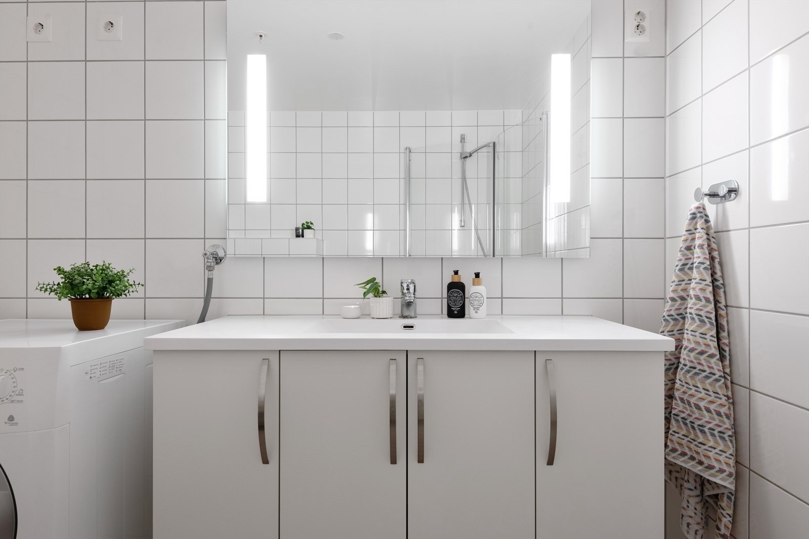 Badet har flotte fliser med gulvvarme. Innredningen består av vegghengt toalett, dusjhjørne med svingbare glassdører, servant med skapinnredning og speil med belysning over servant Galleribilde