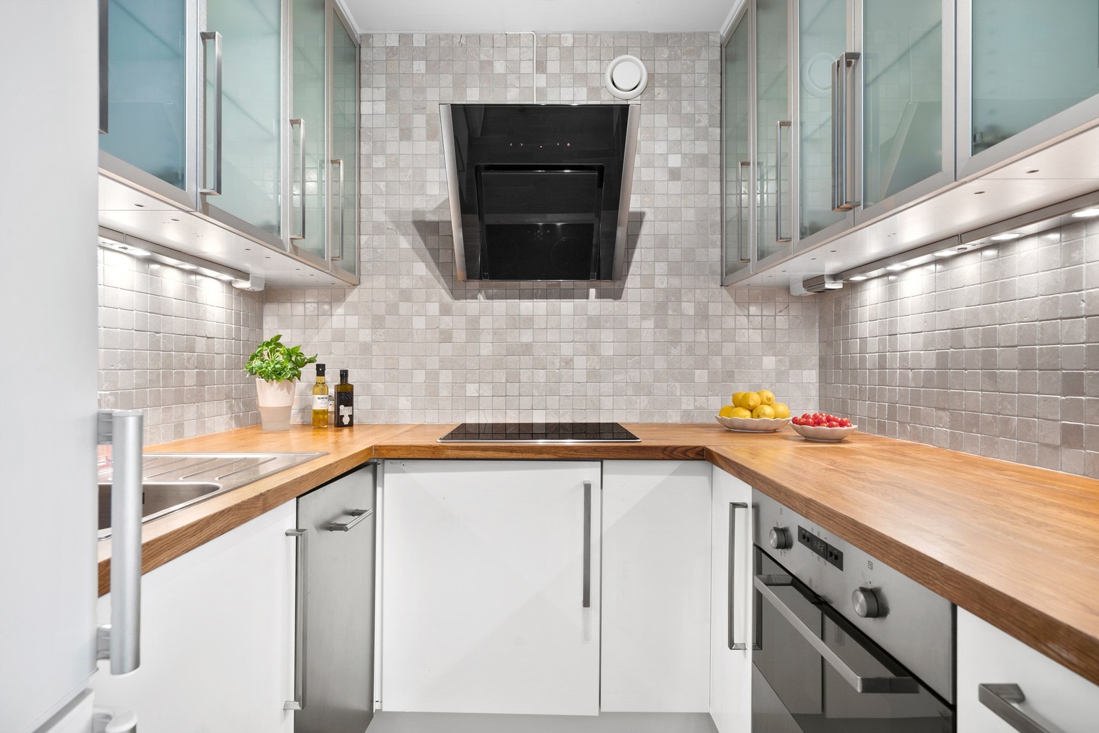 Kjøkkeninnredning med hvite fronter og håndtak i stål. Benkeplate av heltre eik. Integrert i innredningen er oppvaskmaskin, ovn og platetopp. Galleribilde