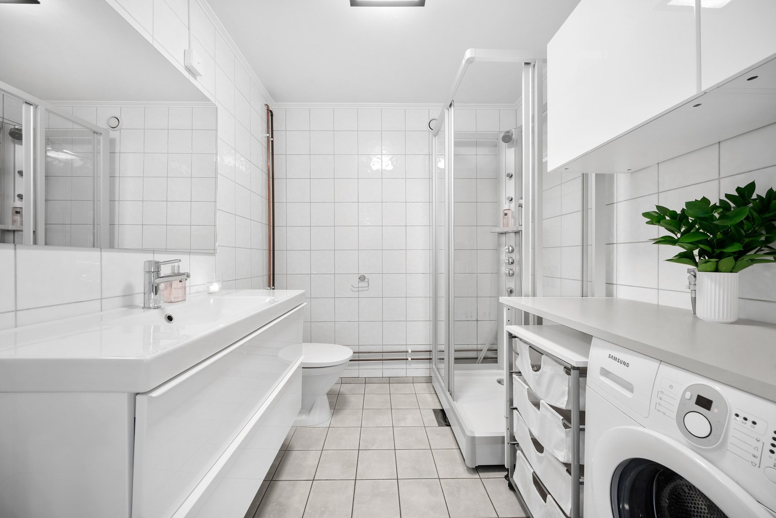 Flislagt bad av god størrelse. Her er det opplegg til vaskemaskin, gulvmontert toalett, dusjkabinett og servant med tilhørende skuffeseksjon. Galleribilde