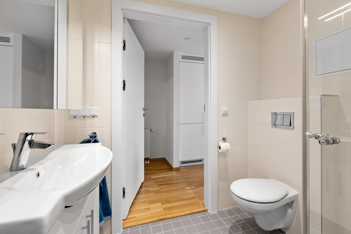 Badet er innredet med dusjhjørne, vegghengt klosett, servant i baderomsinnredning og opplegg for vaskemaskin. Galleribilde