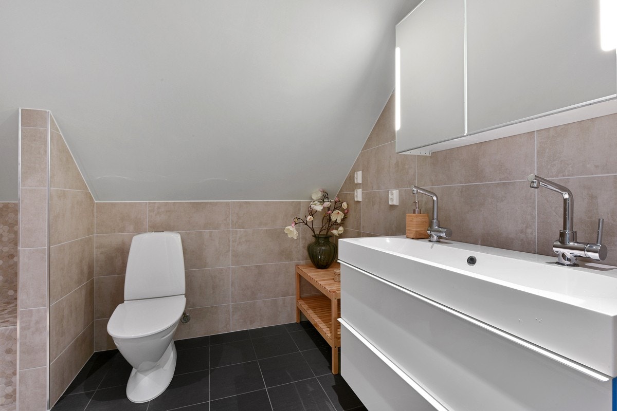 Dusjsonen er flislagt med lyse småfliser, har en flislagt benk og det er både vanlig dusj og regnfallsdusj. Den øvrige baderomsinnredningen består av speilskap med integrert belysning og en hvit skuffeseksjon med heldekkende dobbelservant. Galleribilde