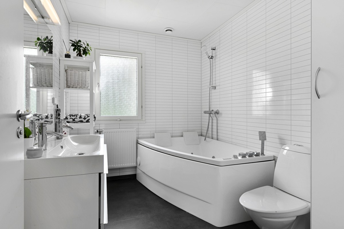 Bad i første etasje med gulvvarme, frittstående toalett og et badekar med nakkestøtter og dusjarmatur. Videre har badet speil med overlys, et hvitt høyskap og en hvit skuffeseksjon med heldekkende dobbelservant. Galleribilde