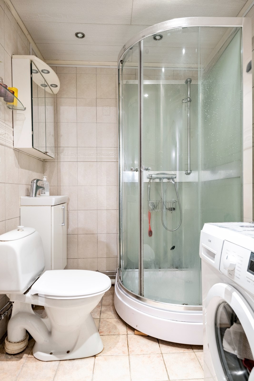 Flislagt baderom med enkel standard. Innredningen består av gulvstående wc, dusjkabinett og servant med underskap, speilskap og belysning Galleribilde