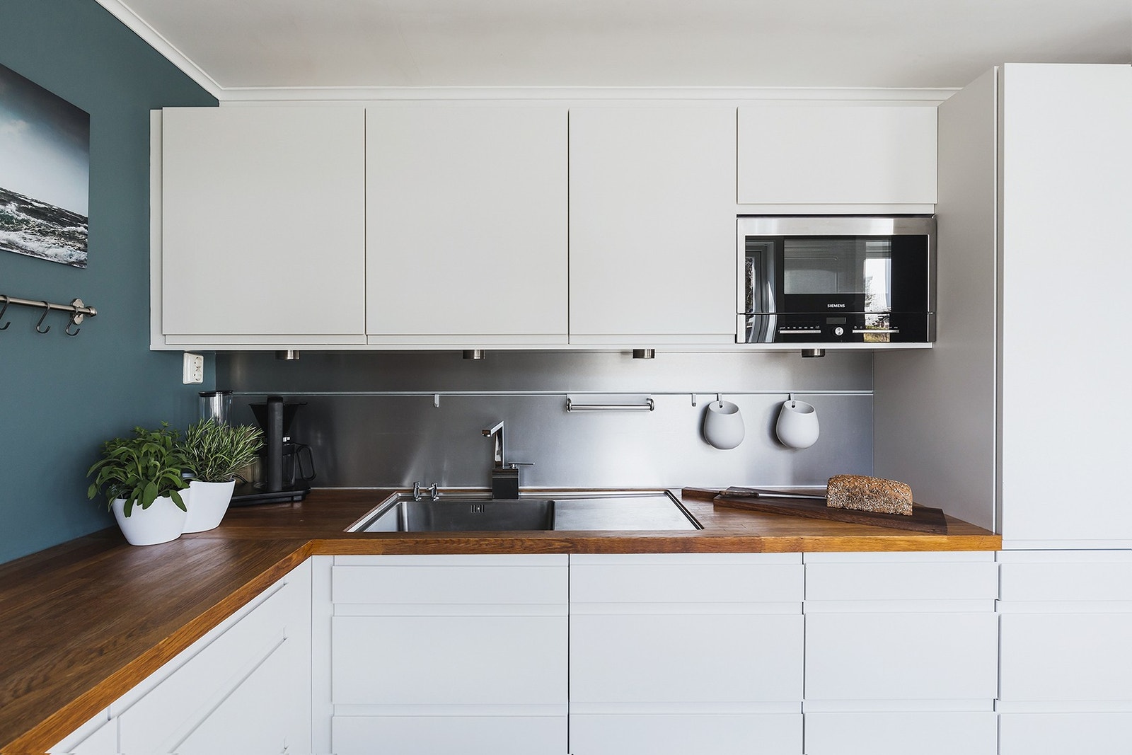 Kjøkkeninnredning fra HTH med glatte fronter, benkeplate i heltre, og aluminiumsbelagte plater på vegger over benkeplate. Galleribilde