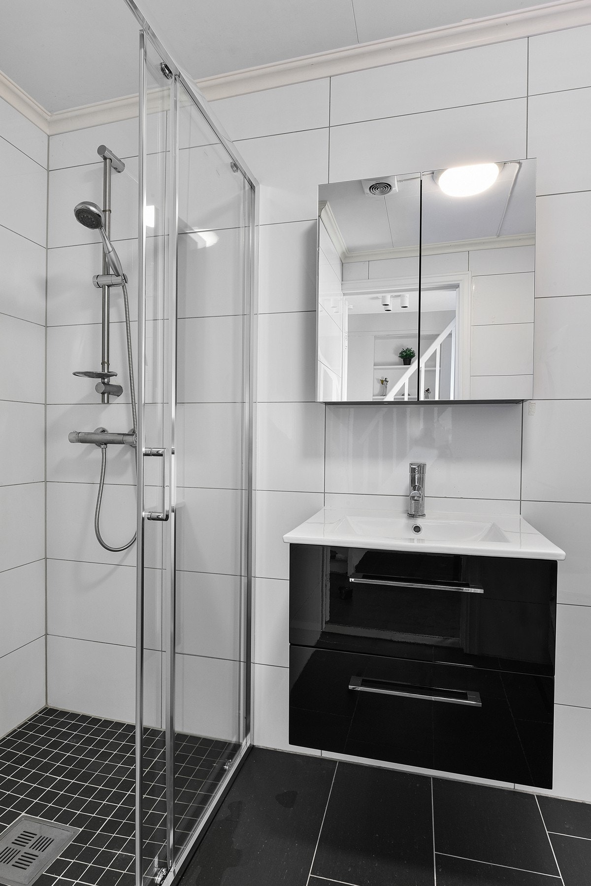 Rommet har speilskap, heldekkende servant på sort skuffemøblement, gulvmontert toalett, samt nedsenket dusjhjørne med mosaikkflis og skyvedører i glass. Galleribilde
