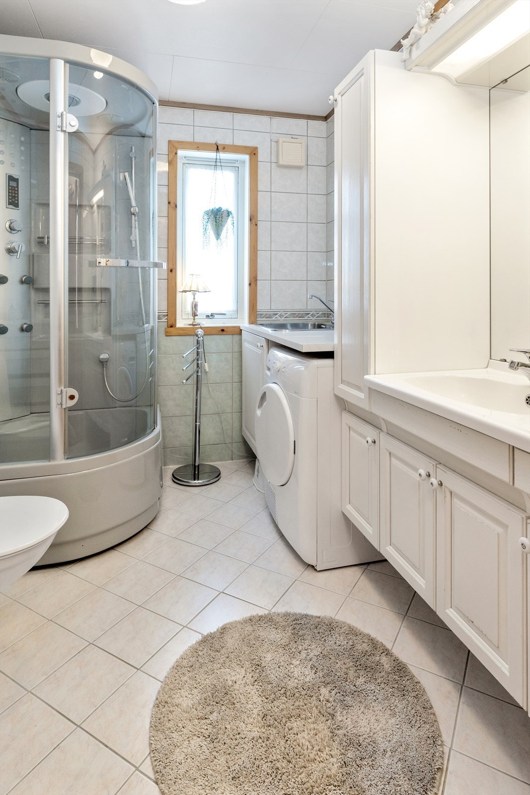 Badet er flislagt, har et romslig dusjkabinett, toalett, opplegg for vaskemaskin og en baderomsinnredning med god lagringsplass. Galleribilde