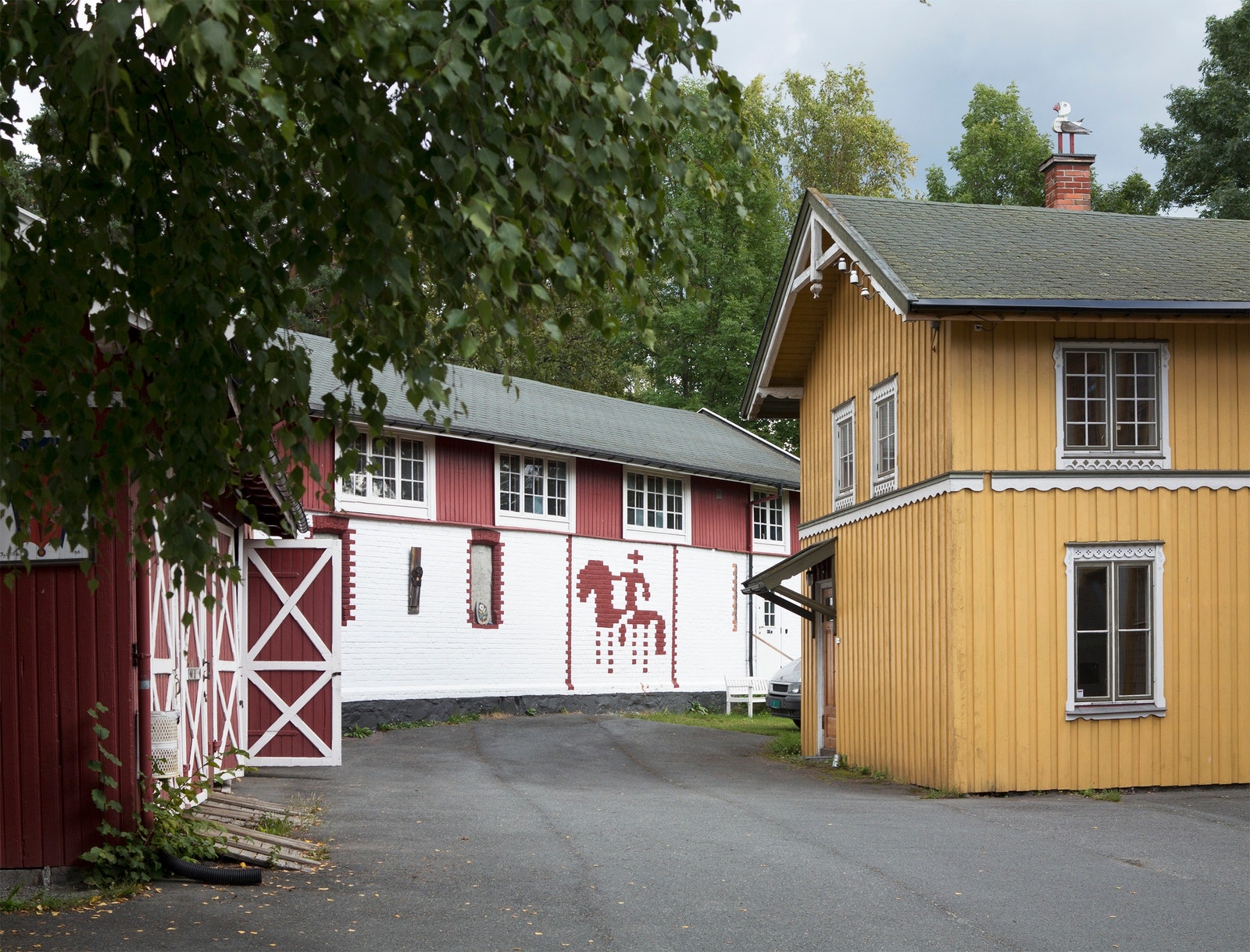 Gårdsplassen, som brukes til uteutstillinger og parkering, med bygningene «Prestens vognskjul» og «Skysstasjonen» Galleribilde