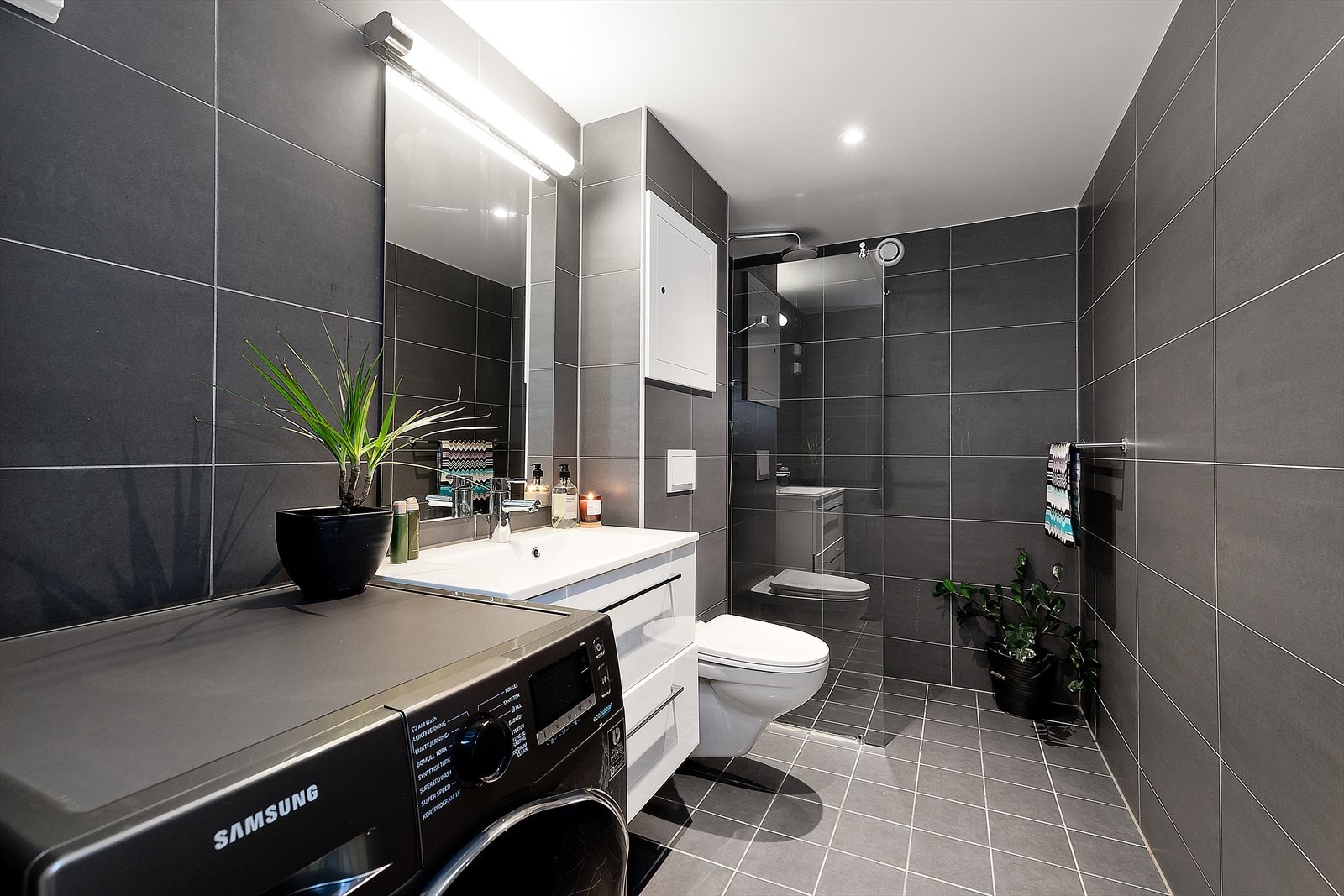 Badet fra 2019 er innredet med mørk flis på gulv og vegg, servantinnredning med speil og overlys, opplegg for vaskemaskin og tørketrommel samt dusjnisje med glassvegg av herdet glass. Rommet har ellers downlights og gulvvarme samt avtrekksvifte. Galleribilde