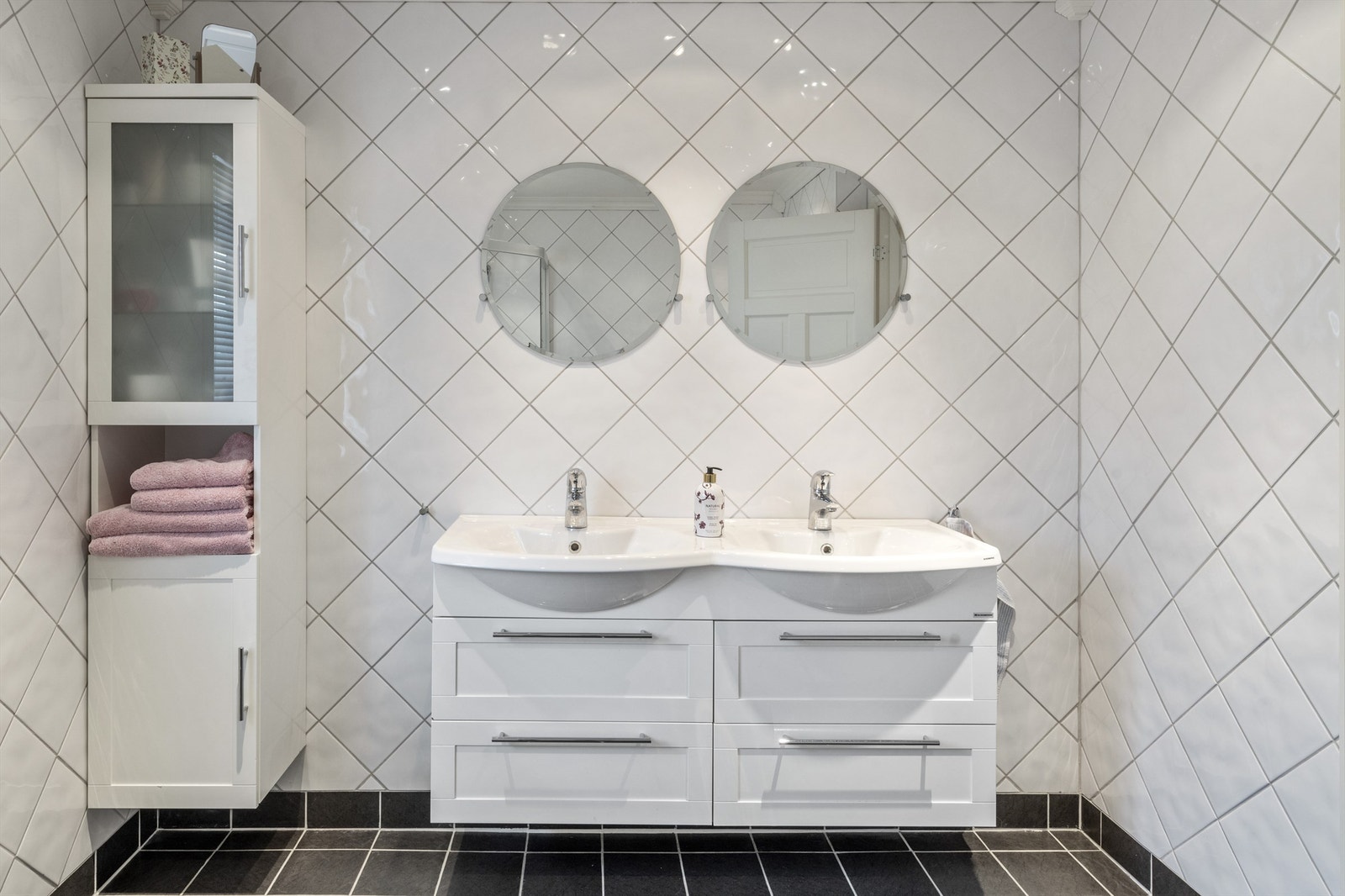 Badet har innredning med heldekkende dobbelservant, høyskap og to runde speil. Ellers er det vegghengt toalett og et dusjhjørne med skyvedør Galleribilde