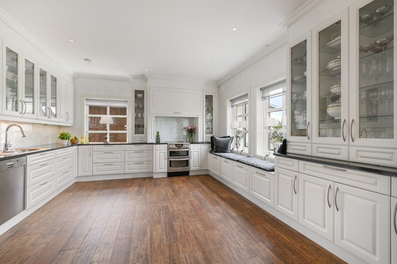 Lekkert kjøkken med innredning som er veltilpasset og hvit, i elegant landlig stil med profilerte fronter, vitrineskap og profiler Galleribilde