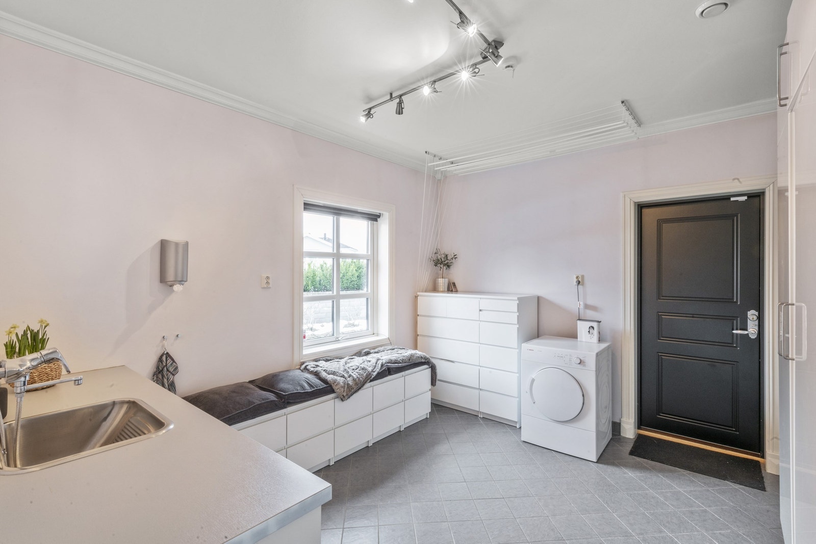 Vaskerommet er romslig med egen inngang. Rommet har fliser på gulv og svak rosafarge på veggene, med skaprekke langs den ene veggen Galleribilde