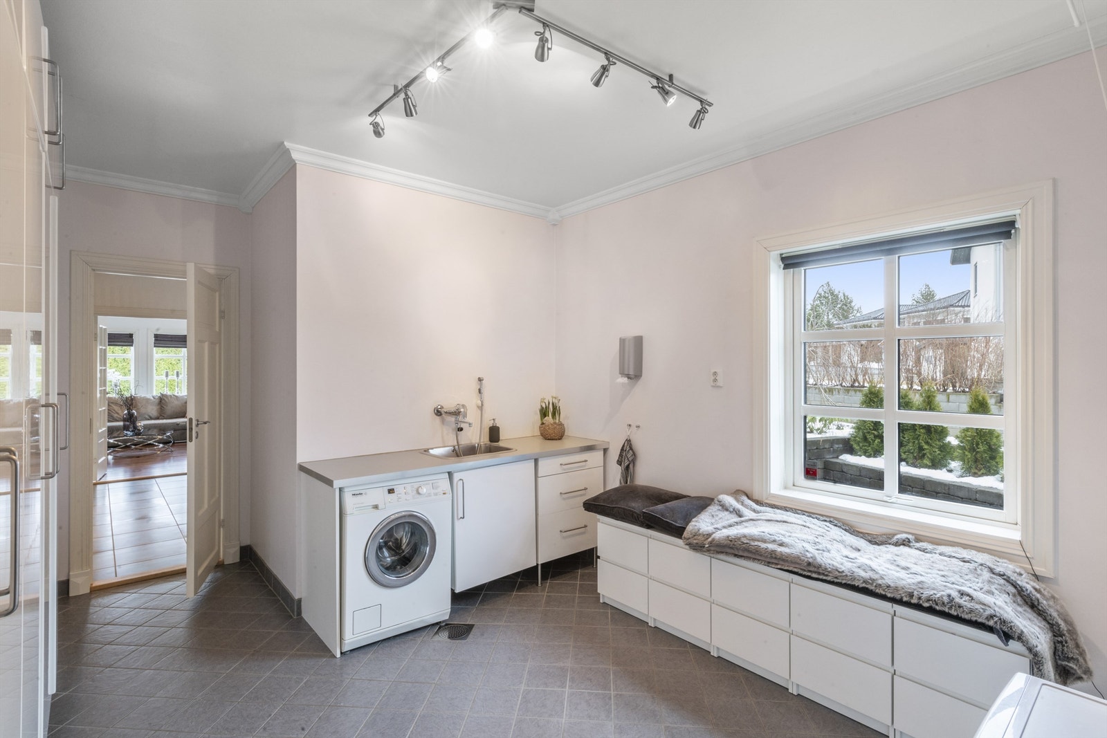 Det er sittebenk i flukt med vinduet, samt et benkeskap med vaskekum og nisje til vaskemaskin under benk Galleribilde