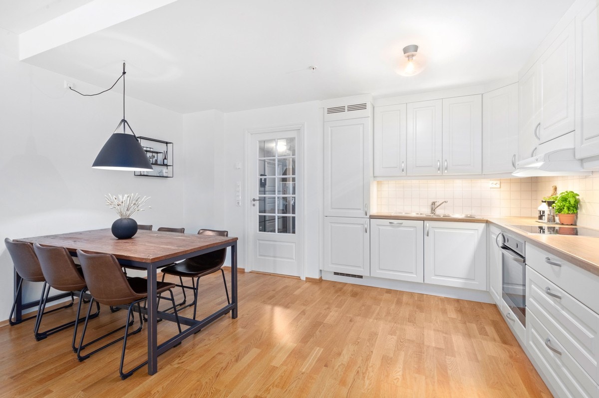 Åpent kjøkken mot stue. Kjøkkenet har hvite profilerte fronter Galleribilde