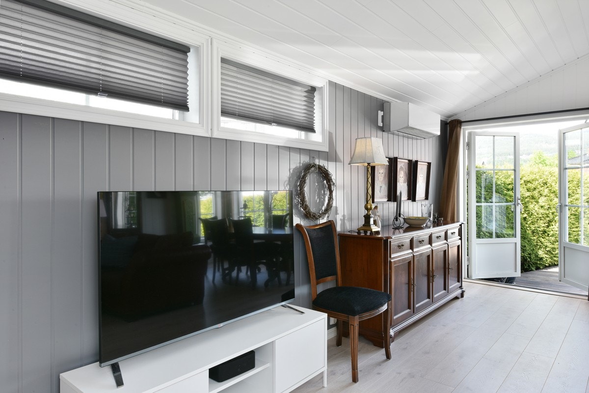 Begge rommene har enstavs laminatgulv og hvitmalt smartpanel på veggene, avbrutt av en gråmalt fondvegg i stuen. Galleribilde