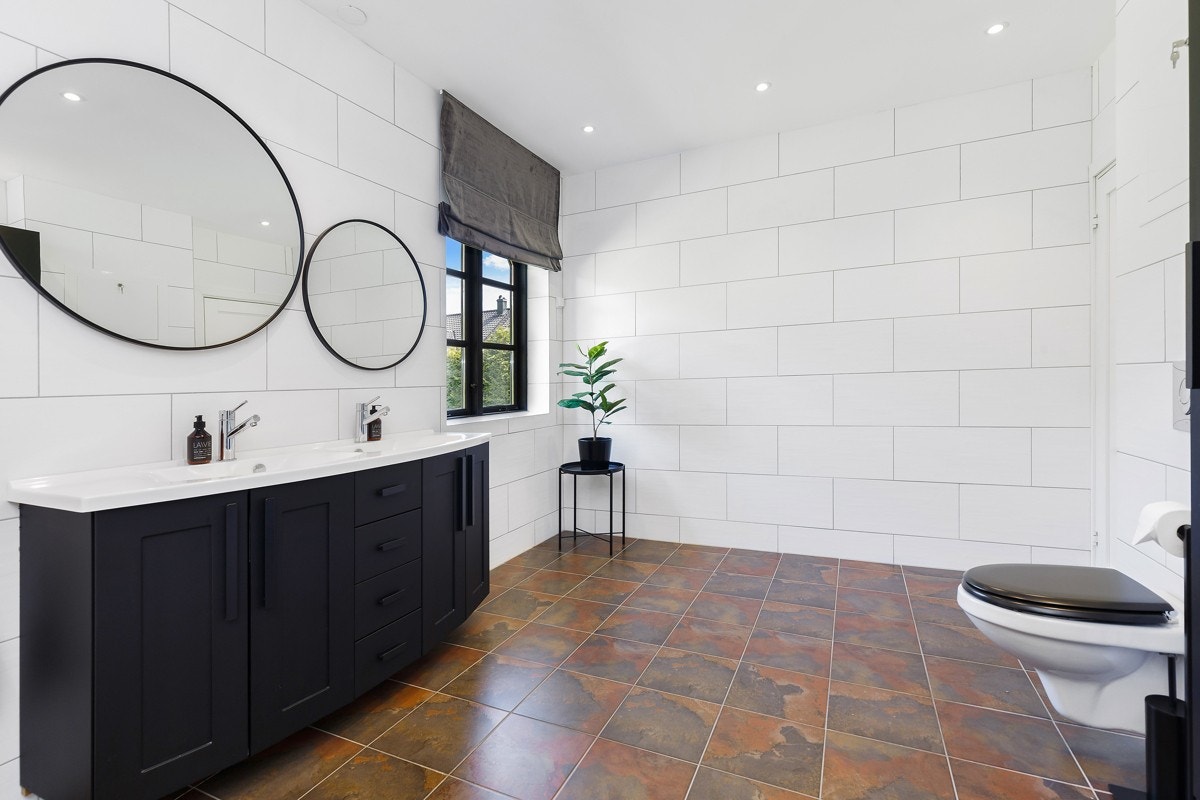 Det er satt inn en sort baderomsinnredning med heldekkende dobbelservant og profilerte skapfronter for oppbevaring av velværeartikler. Galleribilde