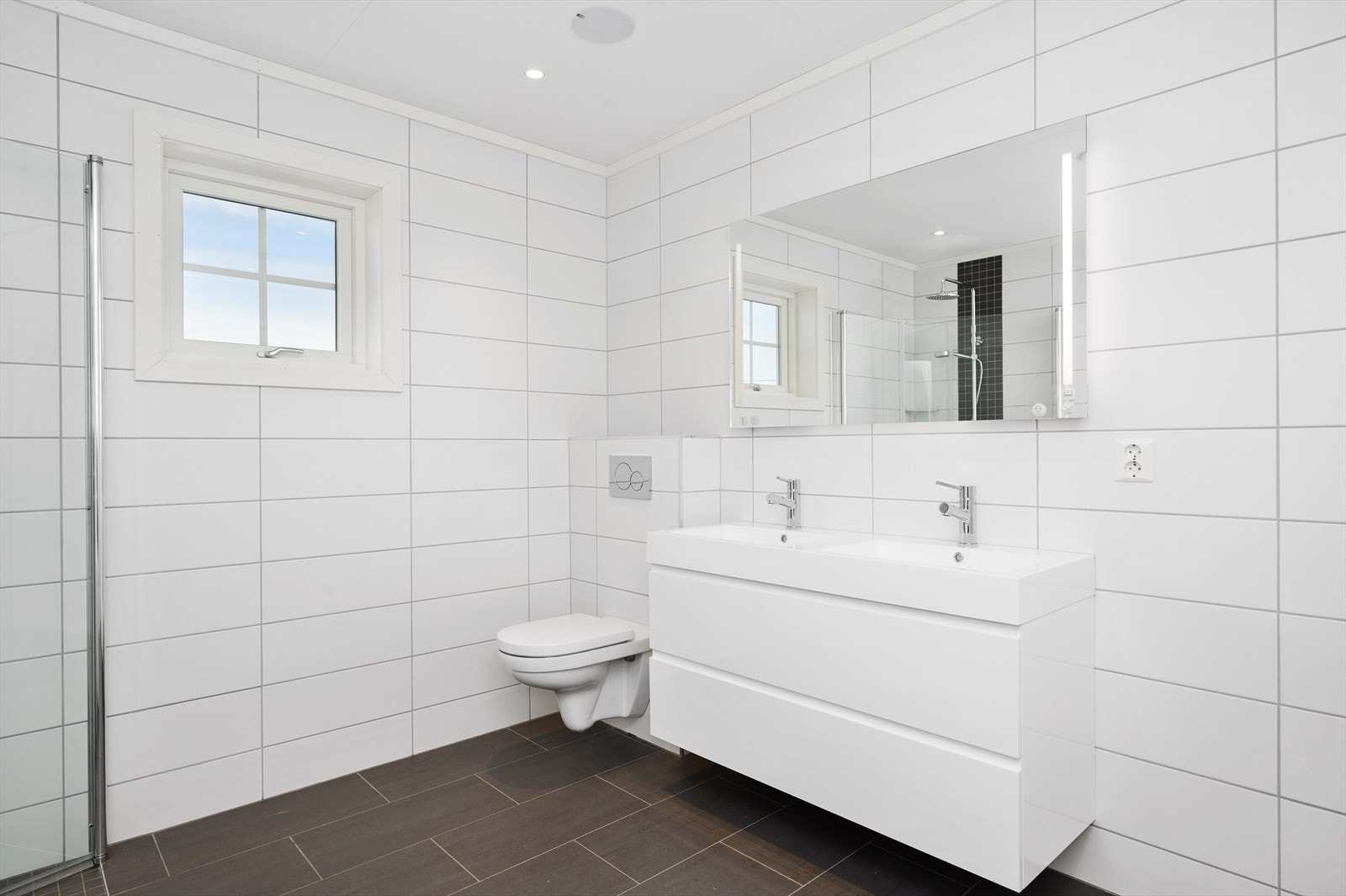 Badet har mørke fliser på gulvet og hvite fliser på veggene. Det er vannbåren varme i gulvet. Galleribilde