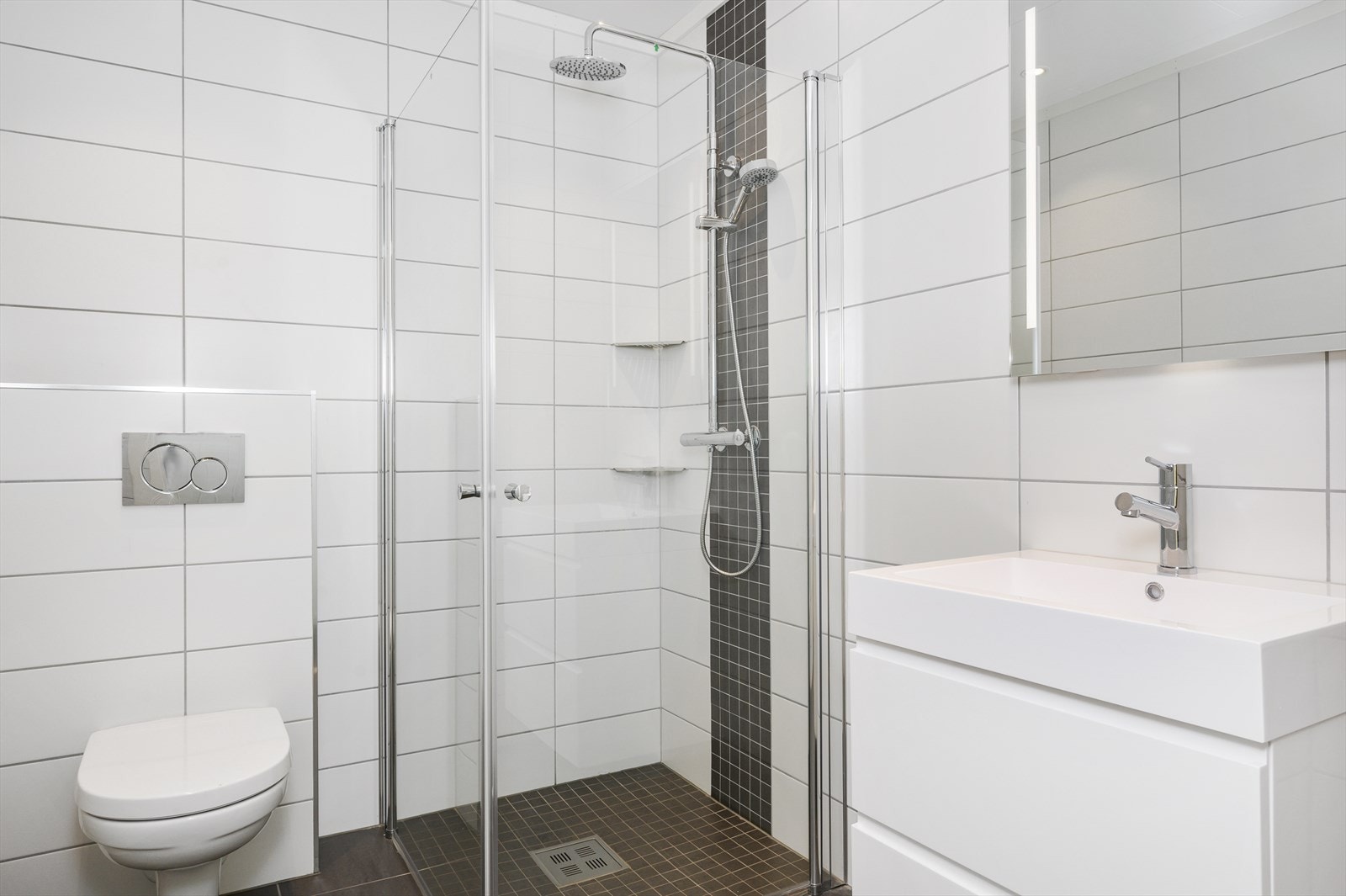 Badet i 1.etg har baderomsinnredning med underskap og speil med lys, vegghengt toalett og dusjhjørne. Galleribilde