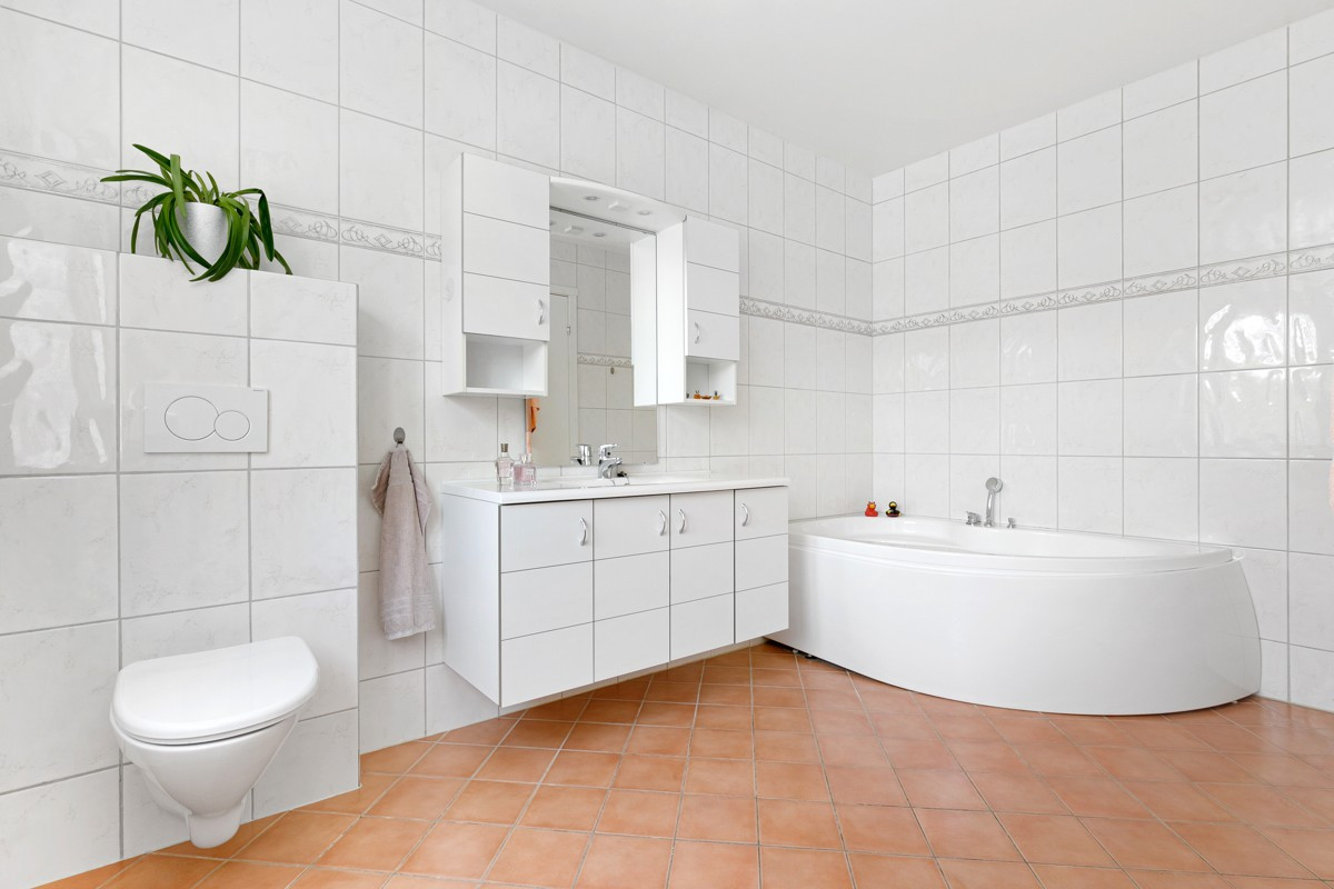 Badet er utstyrt med hjørnebadekar, vegghengt toalett og servant.