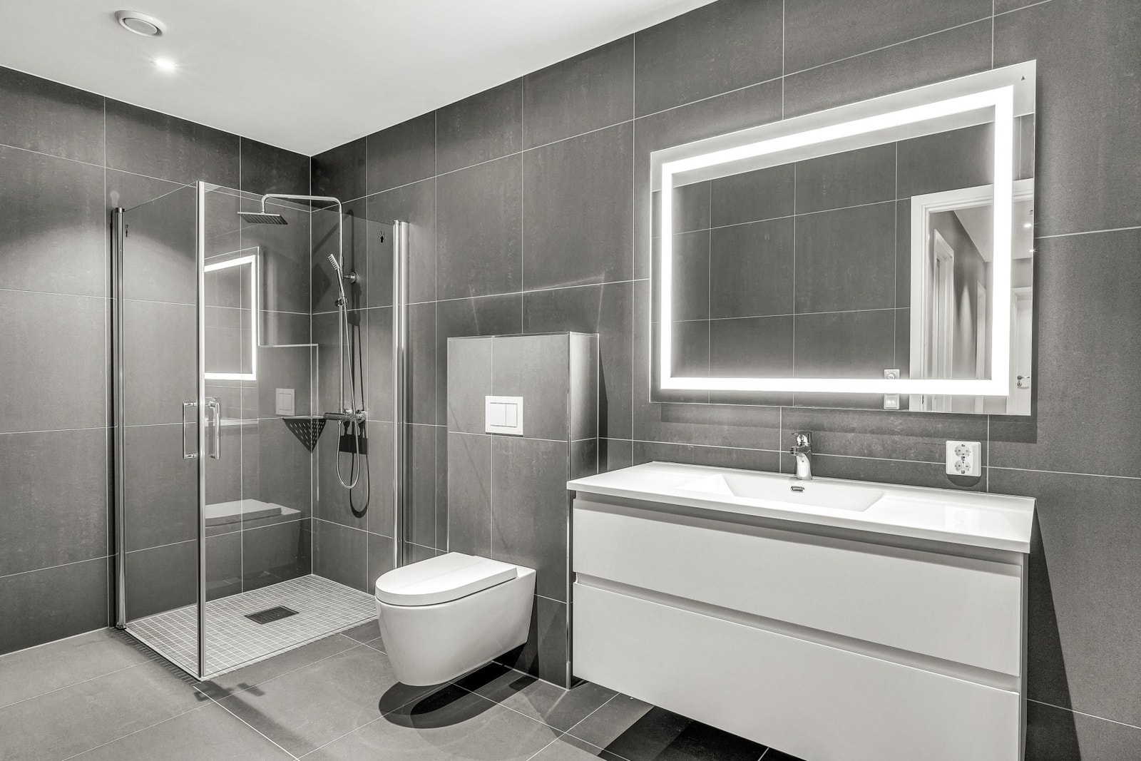 Badene har moderne stilvalg med store 60x60 flis på gulv og vegg. Design-wc, dusjvegger i glass og påkostet dusjarmatur. Galleribilde